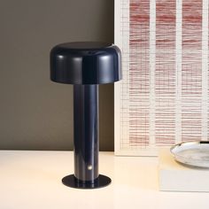 a black table lamp sitting on top of a desk next to a plate and wall paper