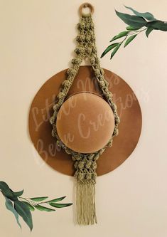 a brown hat hanging on a wall with green leaves around it and a round mirror