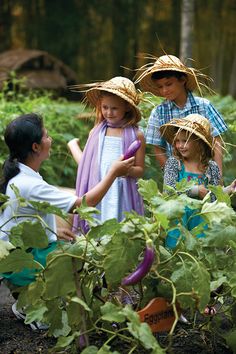 three children are in the garden with their hats on and one girl is holding a plant