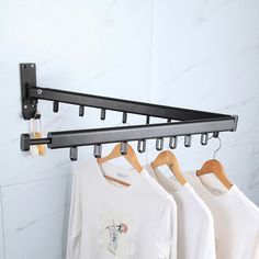 three t - shirts hanging on a rack in front of a white wall with marble tiles