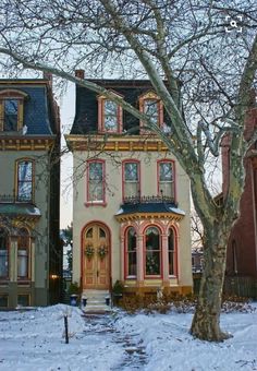 two multi - colored victorian homes in the winter with snow on the ground and bare trees