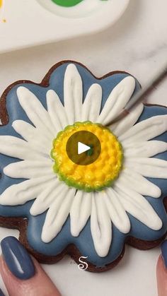 a woman's hand holding a decorated cookie with a flower on it and a video playing in the background