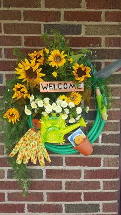 a welcome sign with flowers and gardening tools hanging on a brick wall next to a garden hose