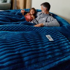 a man and woman laying on top of a blue comforter covered bed in a living room