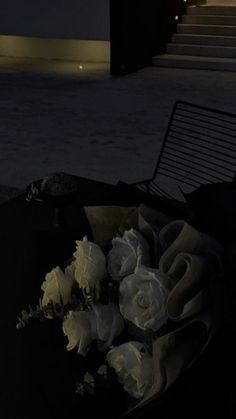 a bouquet of white roses sitting on top of a black table next to a bench