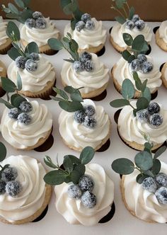 there are many cupcakes with frosting and berries on top that are decorated with greenery