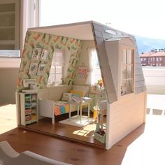 a doll house is sitting on a table in front of a window with the sun shining through it