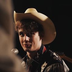 a young man wearing a cowboy hat talking to someone in front of him with a microphone