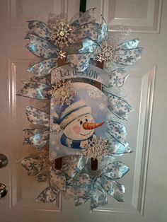 a snowman door hanger on the side of a white door with blue ribbon