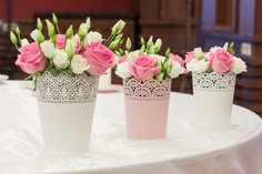 three white vases with pink and white flowers in them on a round table cloth