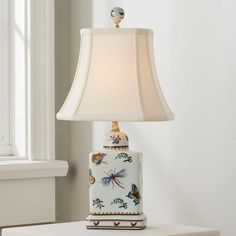 a table lamp sitting on top of a white shelf next to a window with a glass vase