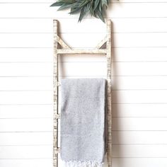 a white towel hanging on a wooden ladder with a green plant in the corner next to it