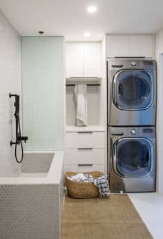 a washer and dryer in a small room with white tile walls, flooring and cabinets