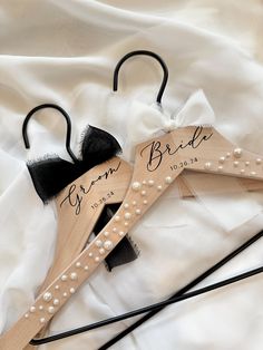 two personalized wooden wedding hangers with pearls and bows on white satin fabric, one for bride and the other for groom