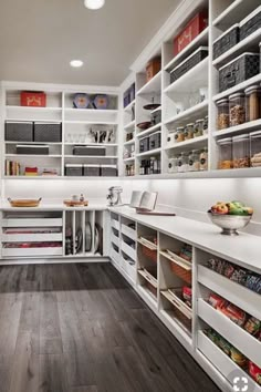 a kitchen with white cabinets and shelves filled with food items on top of wooden floors