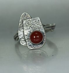 A Modernist Movement ring in silver. I added a 6mm carnelian agate that is all natural stone to the ring. Two artistic modernist silver shapes make up the main part of the ring. I gave them a random texture and applied a dark patina to give the various elements contrast. The band is in silver and are cast from twigs I find on my property I may have cheated a little as I used the twig band which may not exactly be Modernist? This ring was inspired by my recent reading of a book on the modernist jewelry movement. You can order this ring in any size needed. Art Jewelry Ring, Contemporary Art Jewelry, Mans Ring, My Property, Carnelian Agate, Modernist Ring, Modernist Jewelry, Art Jewelry Contemporary, Contemporary Ring