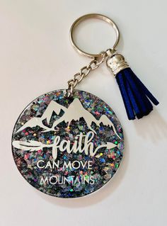 a keychain with the words faith can move mountains on it and a tassel