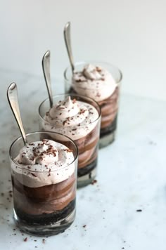 three glasses filled with dessert sitting on top of a white counter next to each other