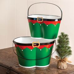 two green and red christmas buckets sitting on top of a wooden table next to a small tree