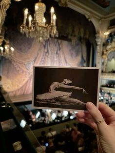 a person holding up an old photo in front of a stage with chandeliers