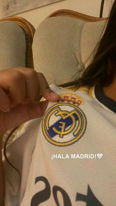 a woman holding onto a jersey with the real madrid logo on it and pointing to her finger