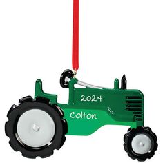 a green tractor ornament hanging from a red cord with the word cotton on it