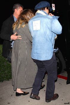 two people standing next to each other in front of a car and one person wearing a hat