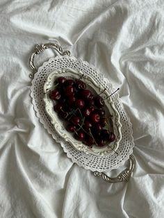 cherries are in a bowl on a white cloth covered tablecloth with an antique silver serving tray