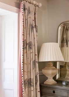 the curtains are pulled back in front of a mirror with a lamp next to it