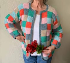 an older woman wearing a colorful cardigan and holding a red rose in her hand