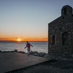 a woman standing on top of a pier next to the ocean at sunset with her arms outstretched