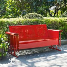 a red park bench sitting next to a bush