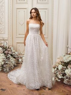 a woman standing in front of flowers wearing a wedding dress