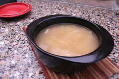 a bowl of soup sitting on top of a wooden board next to a red plate