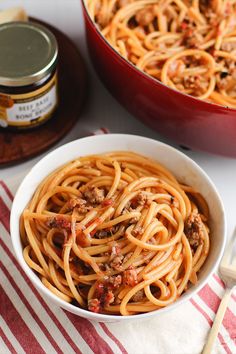 a white bowl filled with spaghetti next to a red and white striped table cloth on top of a wooden cutting board