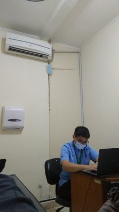 a man sitting in front of a laptop computer wearing a face mask and looking at the screen