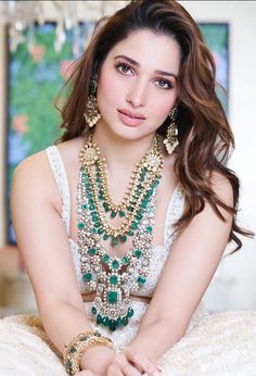 a beautiful young woman sitting on top of a bed wearing green and white necklaces