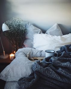 an unmade bed with pillows, blankets and a lamp on the side table next to it