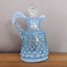 a blue glass pitcher sitting on top of a wooden table next to a gray wall