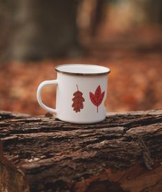 a white coffee cup sitting on top of a tree stump in the woods with red leaves painted on it