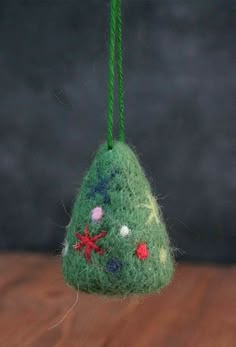 a green christmas tree ornament hanging from a string on a wooden table top