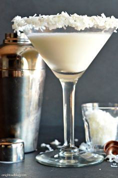 a martini glass filled with white liquid and coconut flakes on the rim next to other glasses