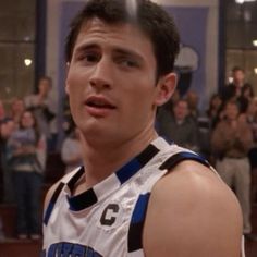 a young man in a basketball uniform is looking at the camera while people are watching him