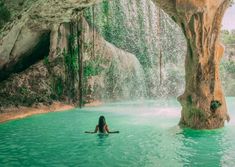 a woman sitting in the middle of a body of water surrounded by large rock formations