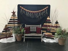 a wooden bench sitting next to potted plants in front of a black wall with a christmas tree on it