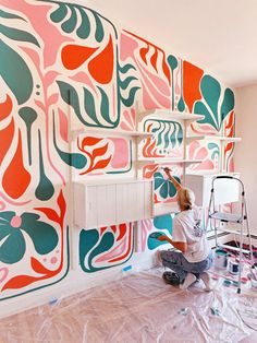 a woman is painting a wall with colorful designs on it and she is kneeling down to paint the walls