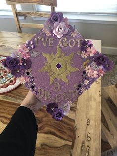 someone holding up a purple graduation cap decorated with flowers