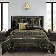 a large bed with black and gold comforters in a room next to two windows