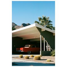 an old red car is parked in front of a house with mountains in the background