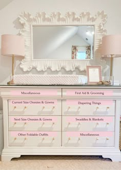 a white dresser with pink drawers and gold trimmings on the top, along with a mirror above it